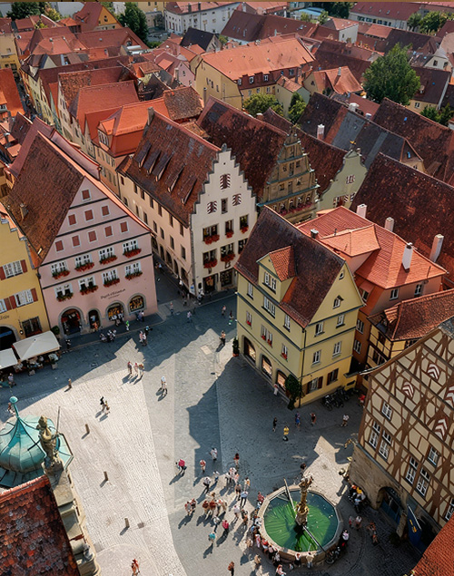 Vogelperspektive auf eine Altstadt mit Fachwerkhäusern und einem Platz mit Brunnen.