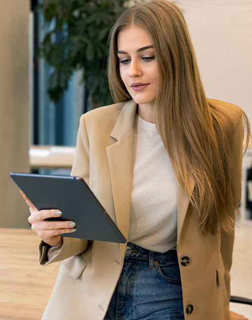 Frau in Blazer in Büro blickt auf digitales Tablet.
